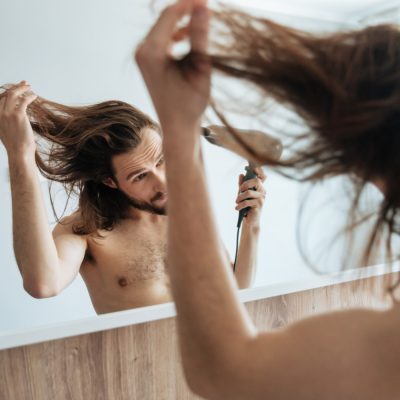Muž dívá do zrcadla a fénuje si vlasy